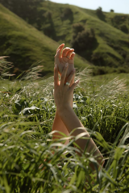 Two hands reaching up from tall grass toward hills